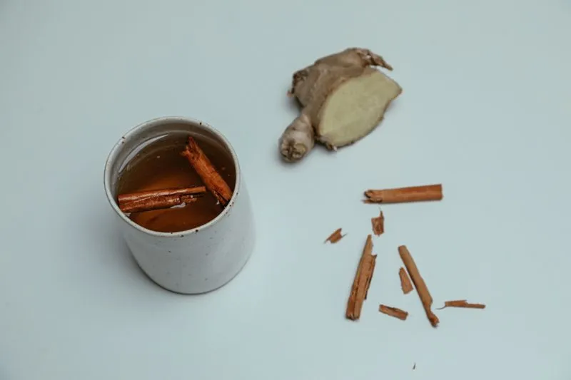 Fresh ginger root cut in half beside a mug of tea with cinnamon sticks