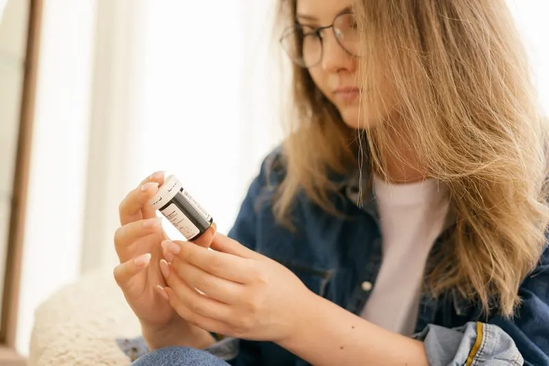 Young woman in glasses reading the label on a medicine bottle at home