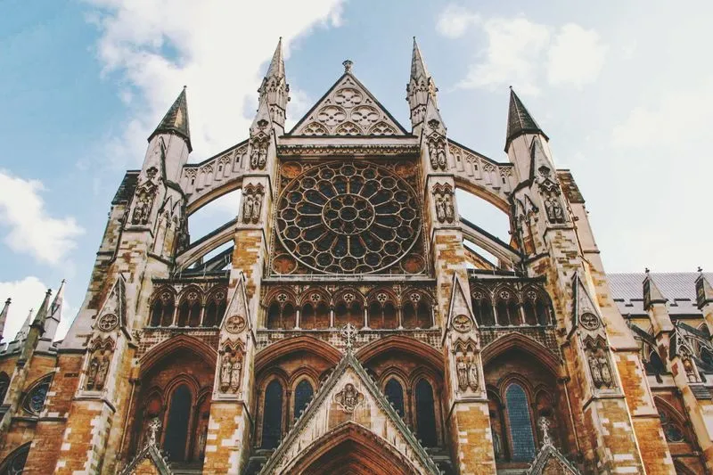 The Gothic façade of Westminster Abbey and its great rose window, seen from below against a blue sky streaked with cloud
