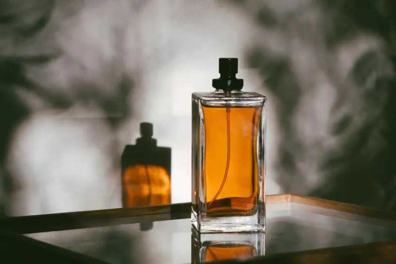 Glass perfume bottle filled with amber liquid on a mirrored tray in warm light, with its reflection