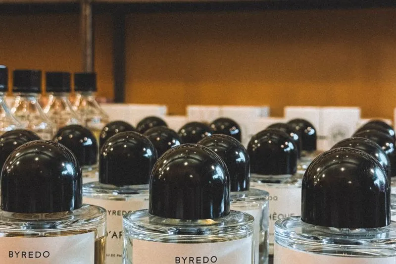 Rows of same-shaped perfume bottles from one brand, with rounded black caps, lined up on a shop display