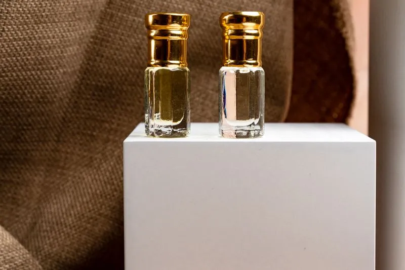 Two miniature perfume bottles with gold caps standing on a white plinth