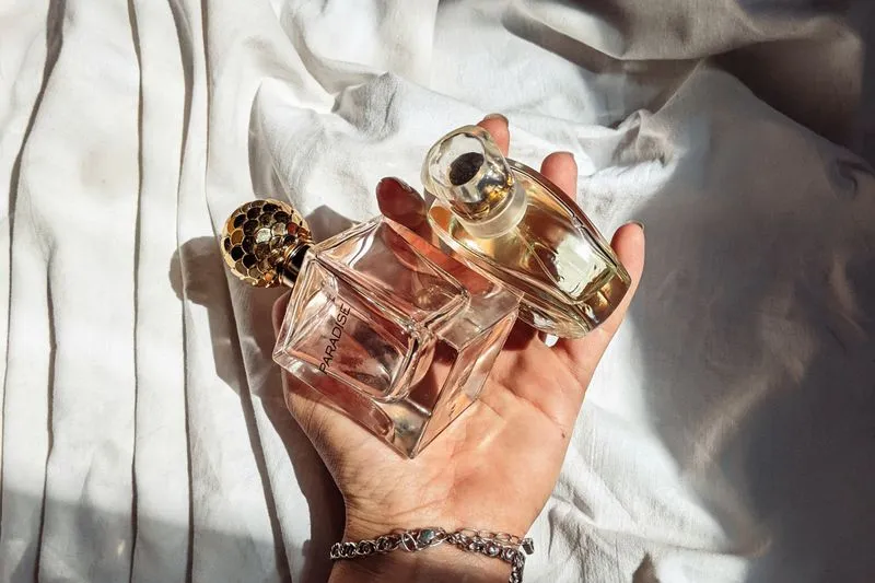 A hand holds two different perfume bottles, one in front of the other, in daylight