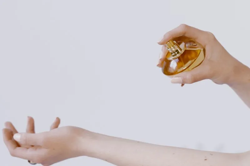 Woman spraying perfume over the inside of her forearm, holding the bottle well away from the skin