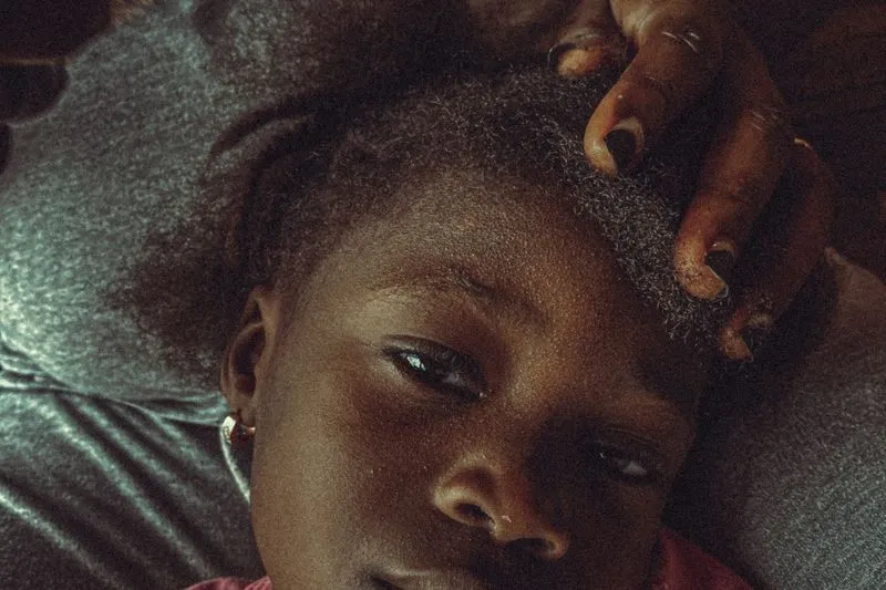 An adult's hand gently parting a little girl's hair near the crown of her head