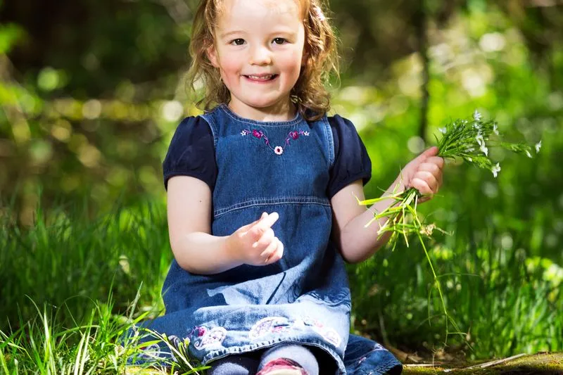 Little girl sitting in the grass, holding a small bunch of wild flowers