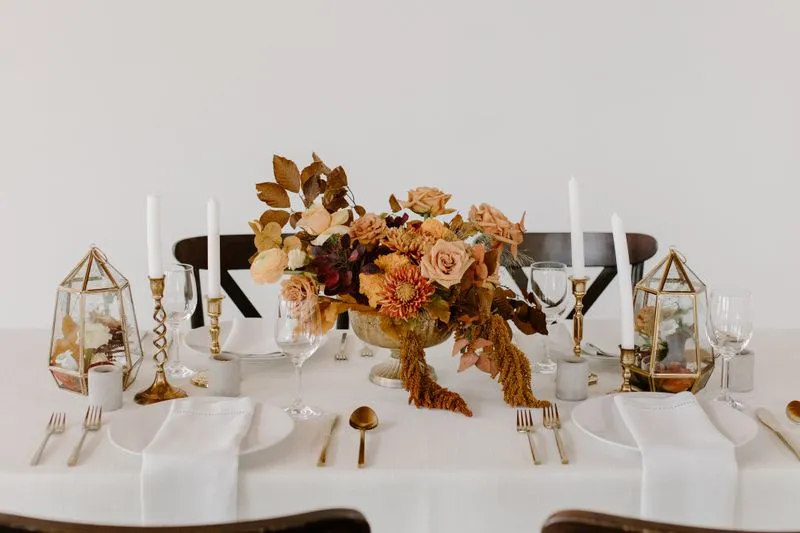 Table set with tall candles, stemmed glasses and a copper-toned flower arrangement