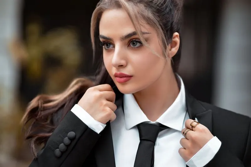 Portrait of a woman in a black jacket, white shirt and tie, hand at the collar