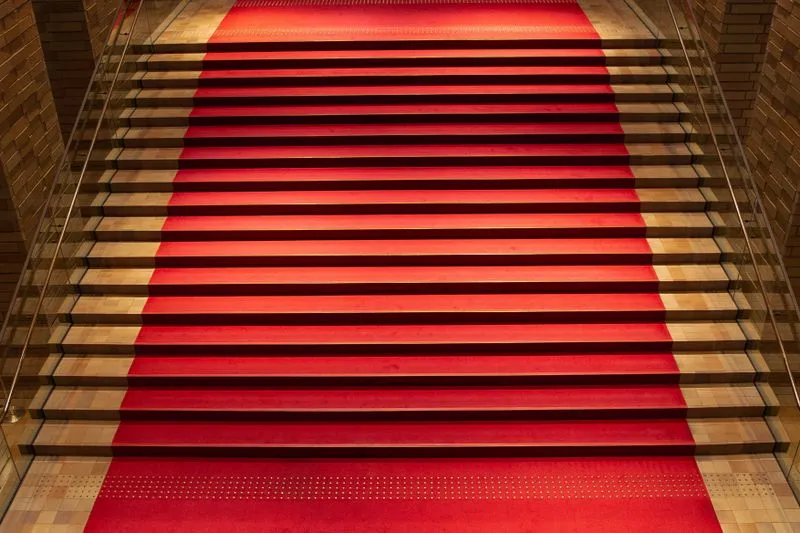 Red carpet runner laid over an indoor staircase, between glass railings and warm light
