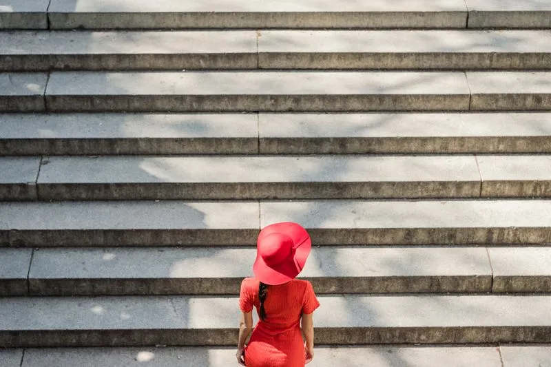 Woman in a red dress and wide-brimmed hat climbing a wide stone staircase