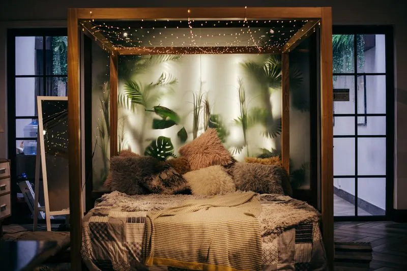 Wooden four-poster bed at night, lit by a string of fairy lights strung overhead against a backdrop of plants