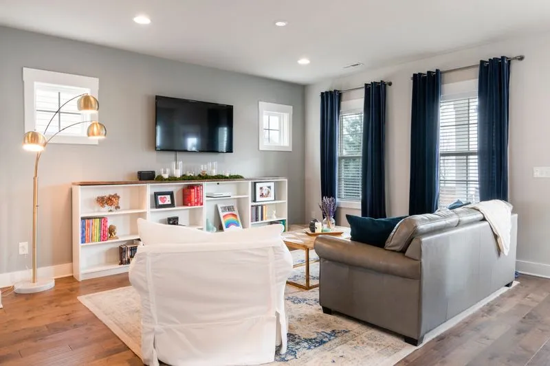 Bright living room with a patterned rug on wood flooring, a white slip-covered armchair, a grey leather sofa and navy curtains