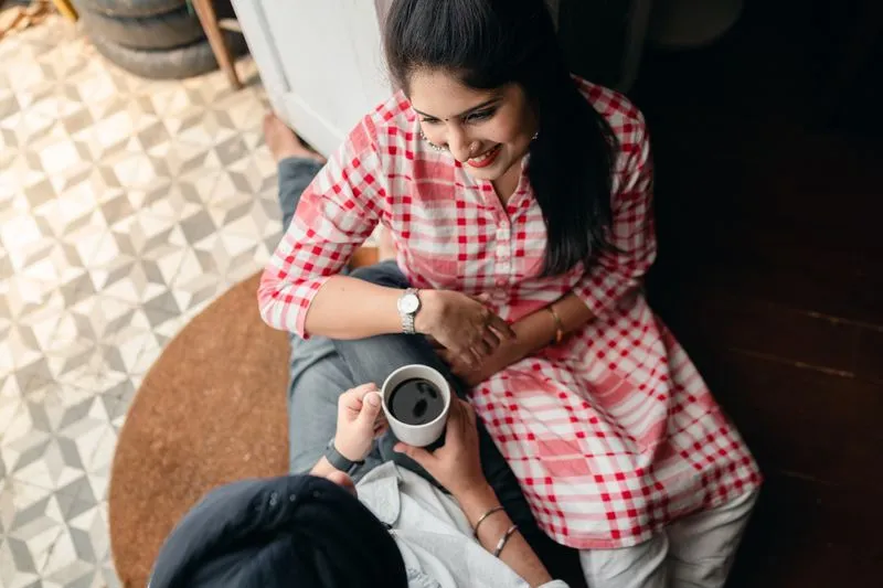Smiling young woman leaning against her partner, who is holding a mug, a warm moment at home