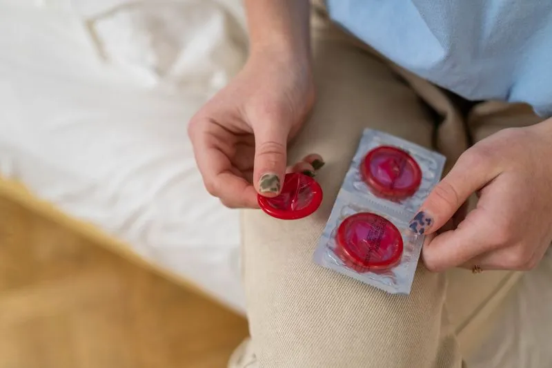 Hands holding an unwrapped condom next to a still-sealed wrapper