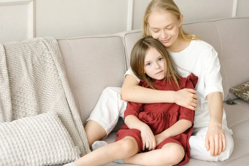 A mother and daughter sitting on a sofa, the mother giving her daughter a gentle hug