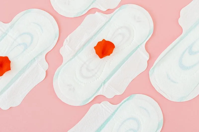 Several sanitary pads laid out on a pink background, some with a red flower petal on them