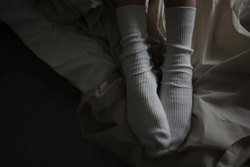 Feet in white cotton socks resting on a pale duvet