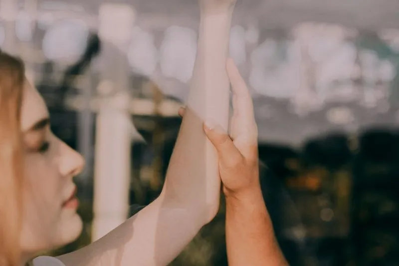 A hand touching the inside of a woman's raised forearm in golden light