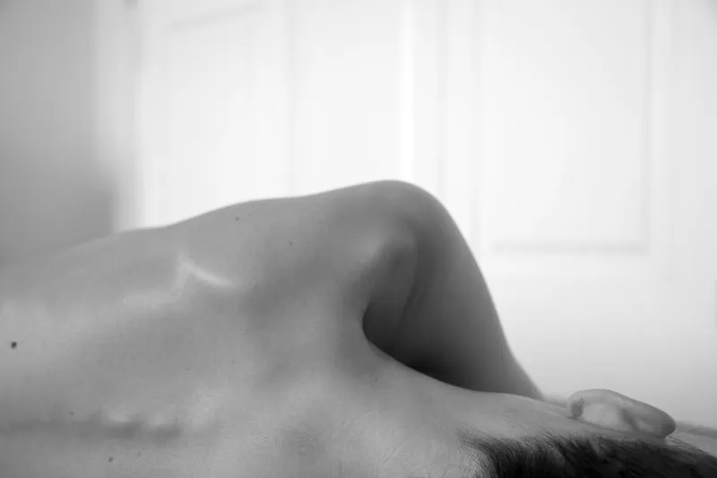Black-and-white close-up of a woman's bare shoulder and upper back as she lies down