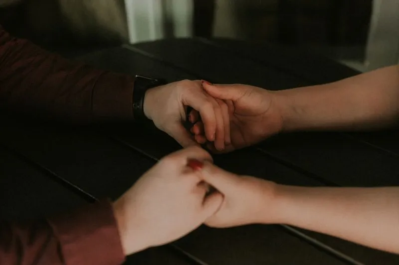 Two people holding hands across a dark table in dim light