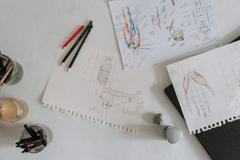 Annotated anatomical sketches of a hand and foot with coloured pencils resting on a bright desk