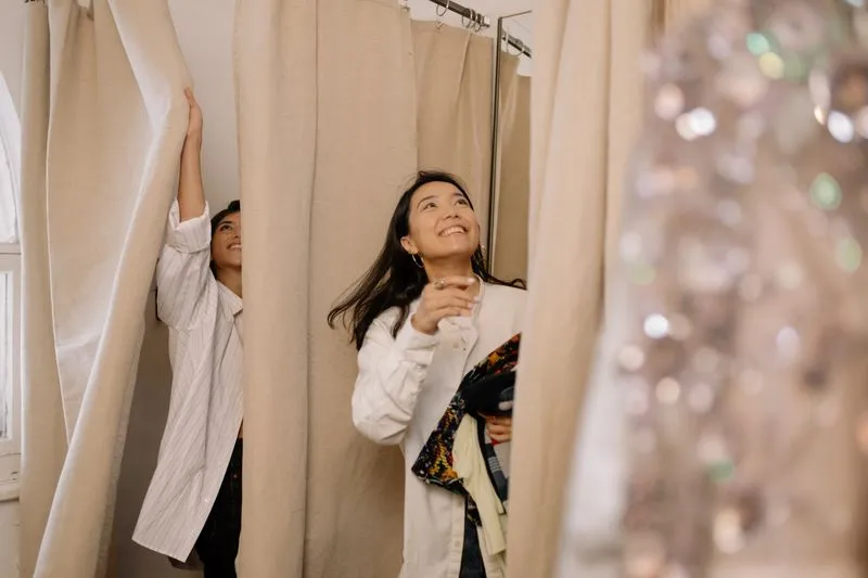 Two customers trying on clothes in a beige-curtained fitting room