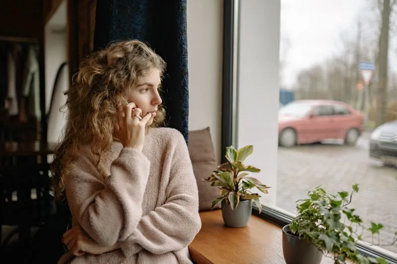 Woman sitting on a window seat with a phone to her ear, looking outside