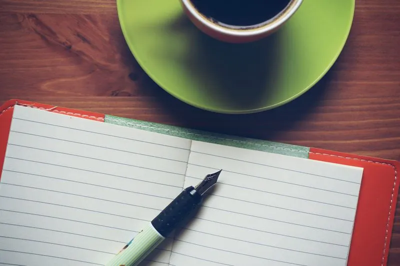 Open paper diary on a desk, next to a pen and a mug