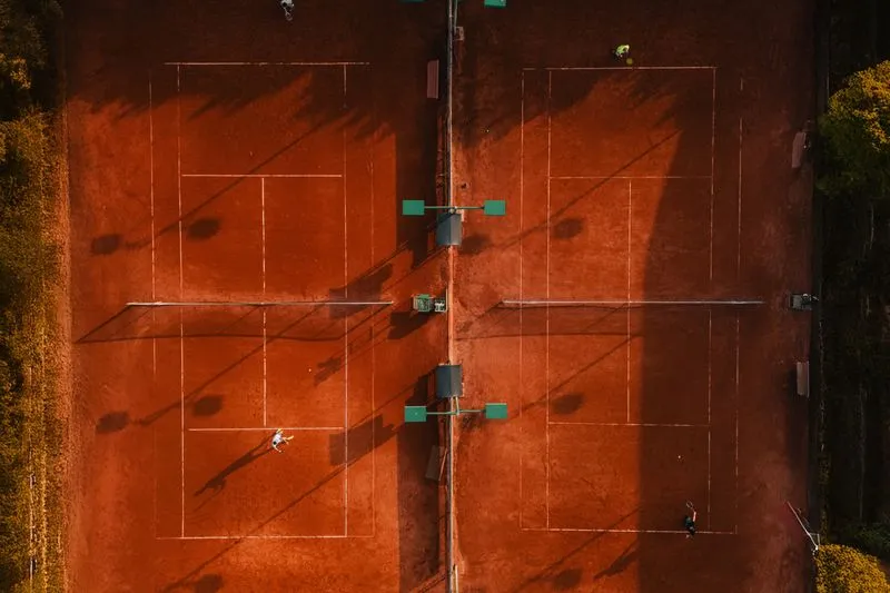 Two orange clay tennis courts seen from above, with players training