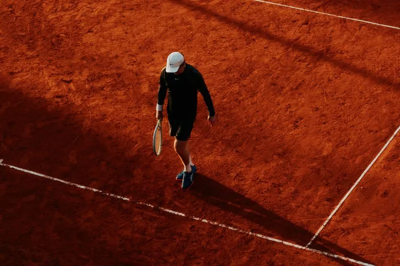 Tennis player seen from above moving across an orange clay court