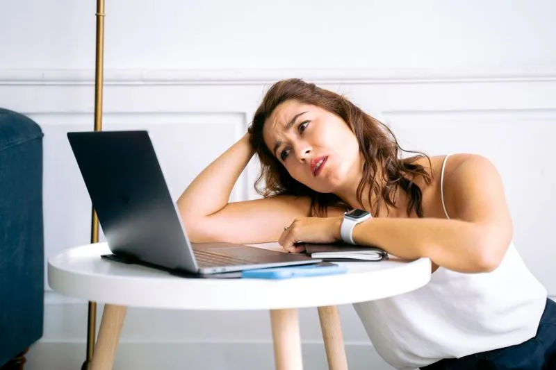 Young woman sitting at a laptop with her chin in her hand, waiting in front of the screen