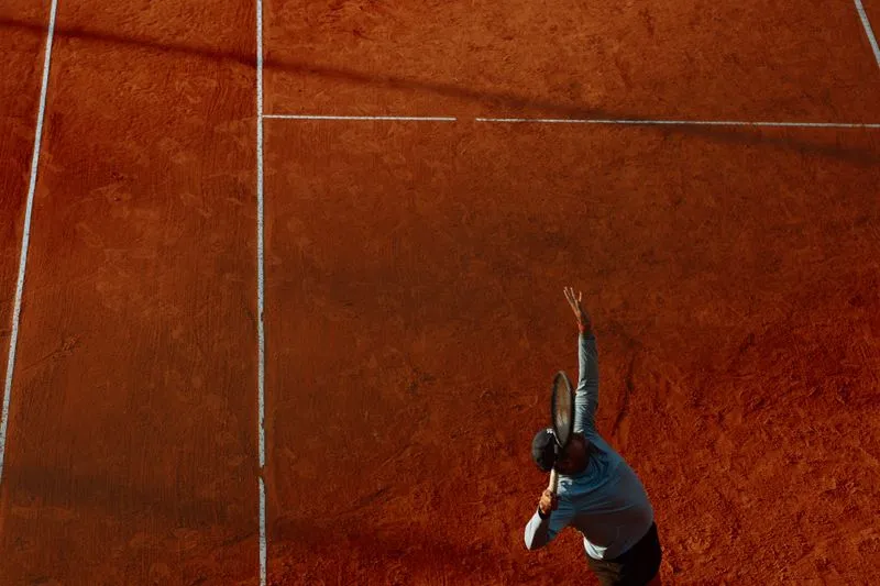 Tennis player seen from above serving on an orange clay court