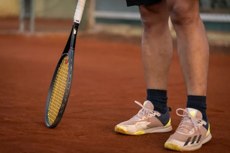 Close-up of a tennis player's legs, clay-dusted trainers and a racket resting on the orange court