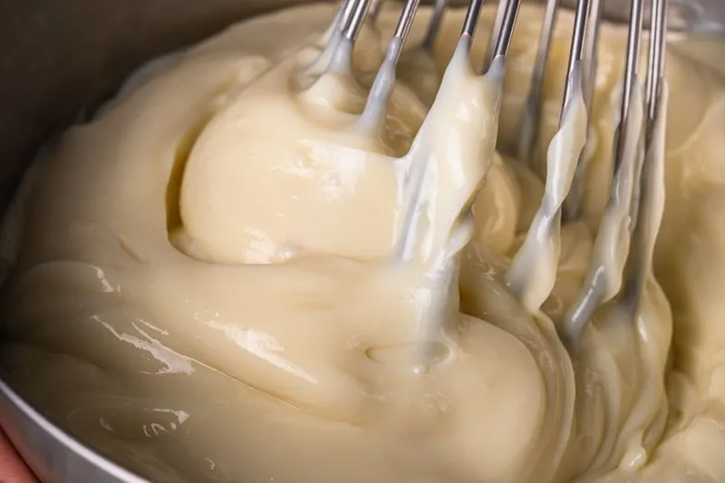 Thick, smooth pastry cream being whisked in a stainless steel bowl