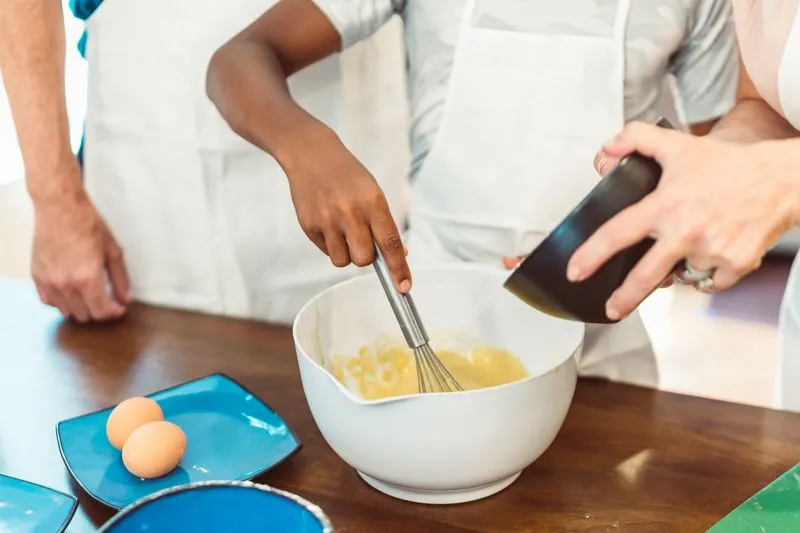 Hands whisking eggs and sugar in a white bowl during a cooking class