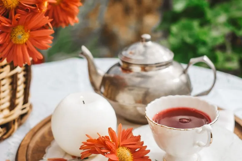 Teapot, cup of red tea and a bunch of orange flowers on a garden table