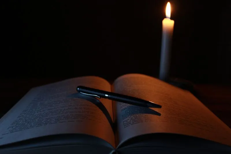 Open notebook and pen on a wooden table beside a lit candle, in the evening