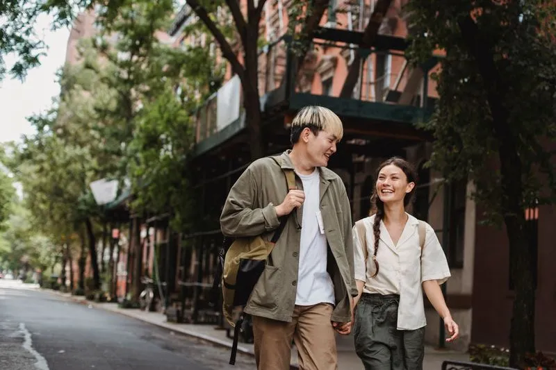 Young couple laughing as they walk side by side down a tree-lined city street