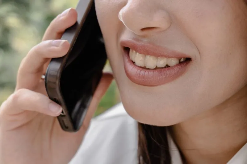 Close-up of a young woman's smile as she laughs on the phone