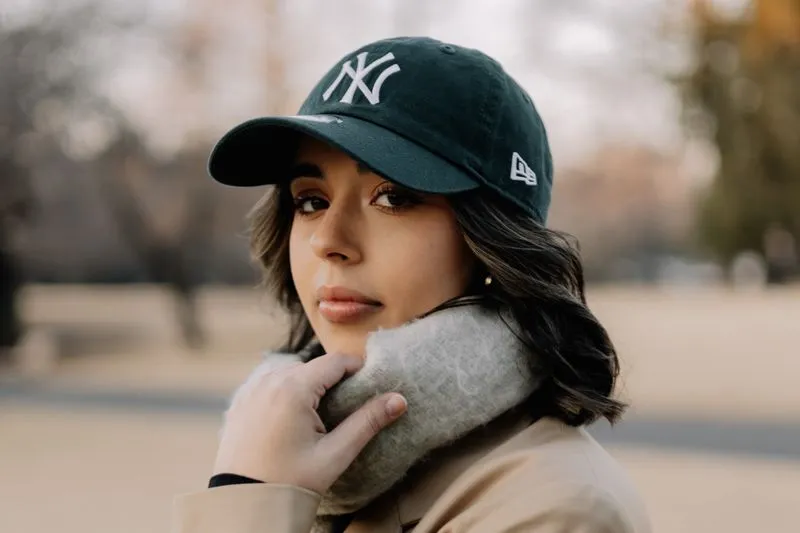 Young woman in a dark green embroidered cotton cap, a grey wool scarf and a beige trench coat, in a park