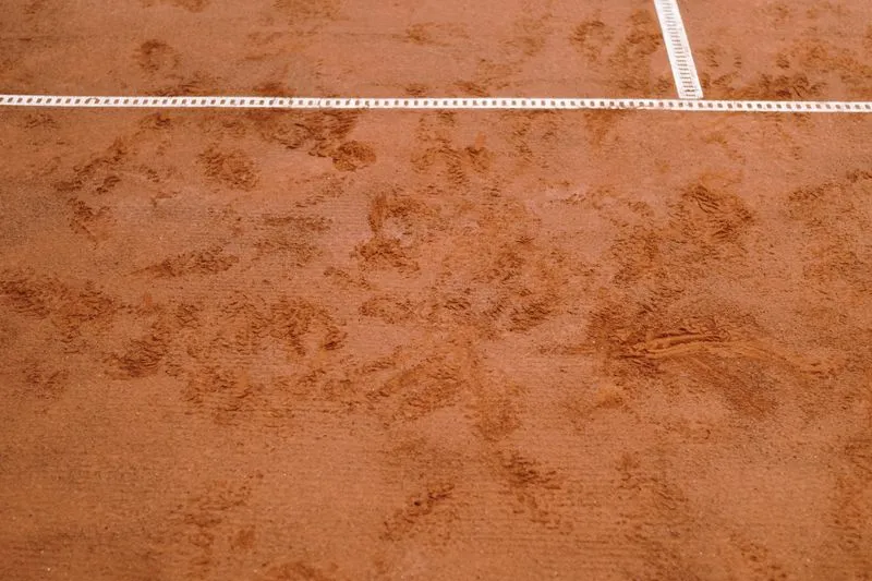 Close-up of a clay tennis court's orange surface, crossed by a white line