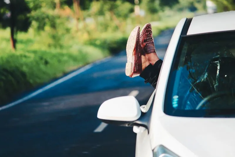 Feet in woven leather loafers, propped out of a car window on a country road