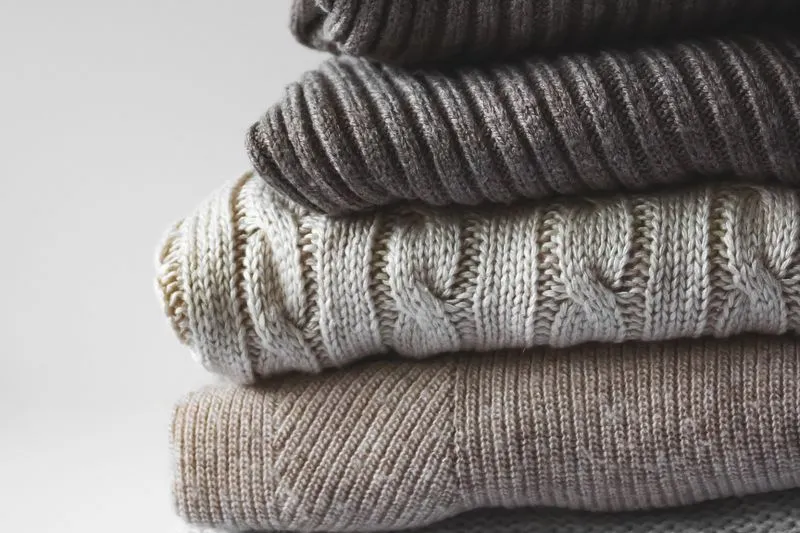 Ecru cable-knit jumper, folded in a stack of wool jumpers