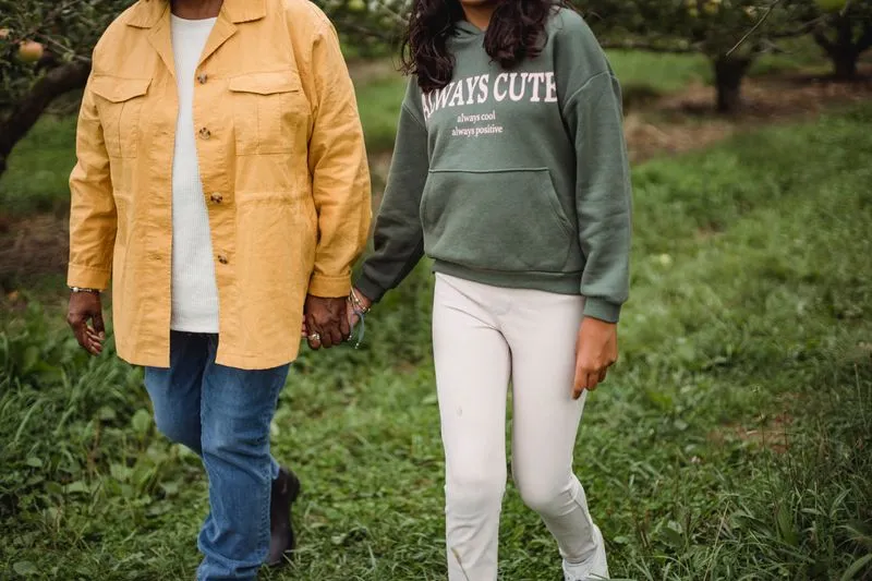 Mother and teenage daughter walking hand in hand along a green path