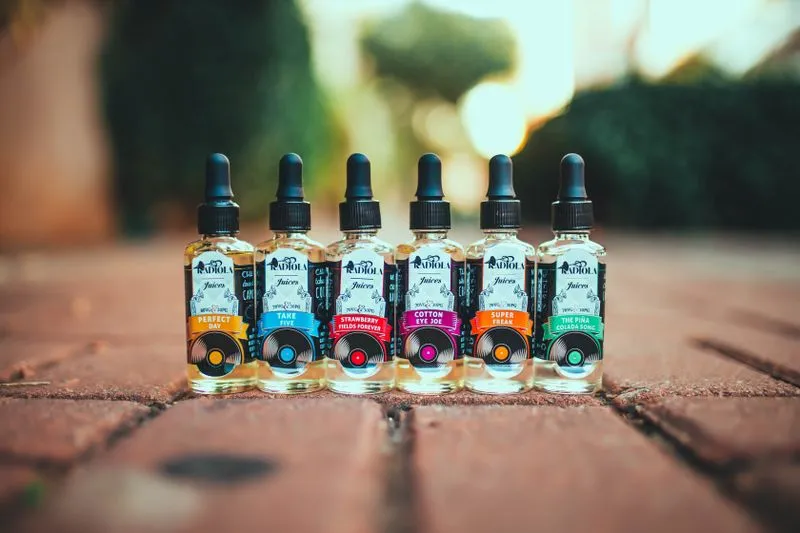 Six e-liquid bottles with colourful labels lined up outdoors