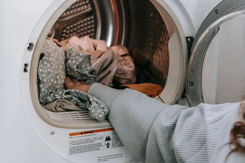Arm in a grey knit sleeve reaching into a front-loading machine full of clothes