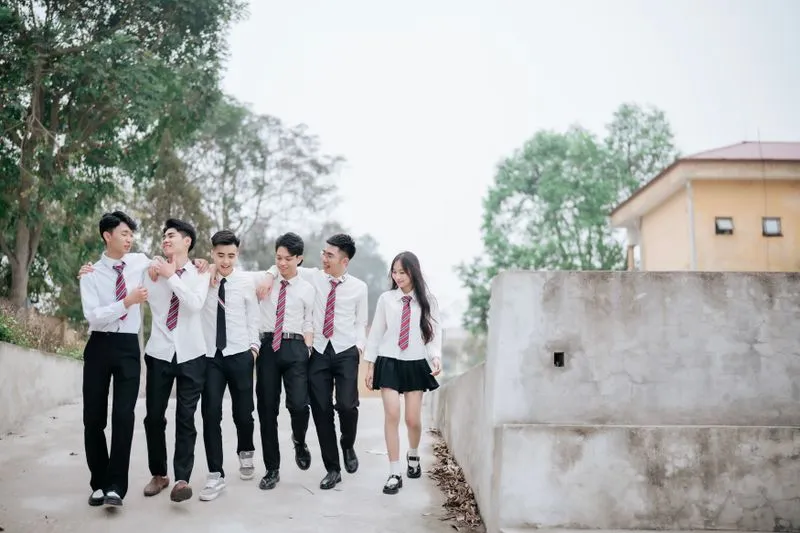 Group of teenagers in school uniform, arms around each other, laughing as they walk
