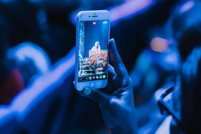 Hand holding a smartphone filming a gig, blue lighting and a blurred crowd in the background