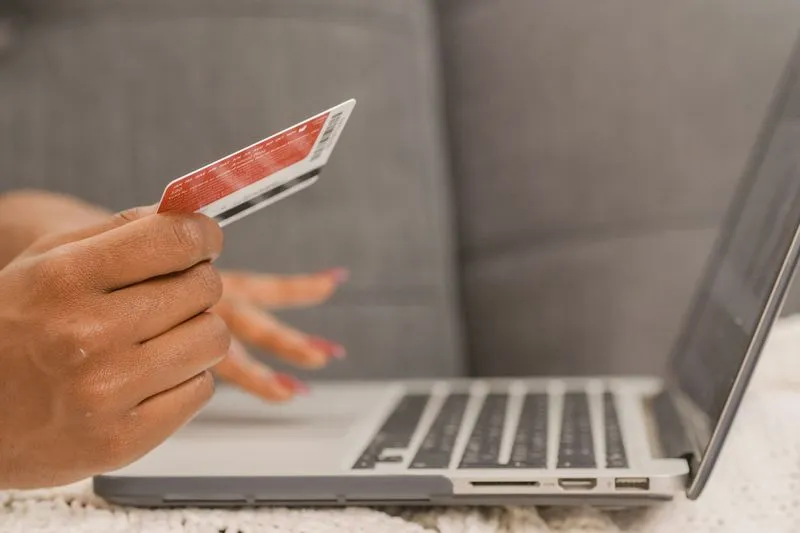 Hand holding a bank card next to a laptop keyboard during an online payment