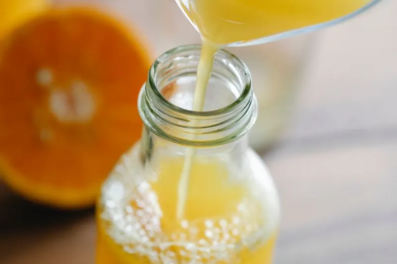 Fresh orange juice being poured into a glass bottle, beside a halved orange